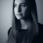 Immagine simbolica di una donna che riflette sulle scelte terapeutiche per il cancro al seno metastatico, con un effetto di luce soffusa che illumina il suo volto pensieroso, lente da ritratto 50mm, duotone blu e grigio per un'atmosfera introspettiva.