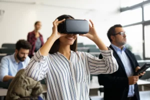 Studenti universitari in un'aula moderna e luminosa. Una studentessa in primo piano indossa un visore VR, sorride leggermente, immersa nell'esperienza. Sullo sfondo, altri studenti e un professore osservano. Prime lens, 35mm, depth of field, luce naturale diffusa che crea un'atmosfera positiva.