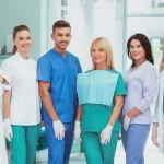 Un team di professionisti del settore dentale (dentisti, igienisti, assistenti) sorridenti e collaborativi in uno studio dentistico moderno e luminoso. La scena trasmette professionalità, supporto e un ambiente di lavoro positivo. Obiettivo prime 35mm, luce naturale brillante, colori vividi, profondità di campo media per mantenere a fuoco il team ma con uno sfondo piacevolmente sfocato.