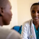 A healthcare provider in Kenya interacting with a young person living with HIV, 35mm portrait, depth of field, focus on connection, clinic setting, soft natural light.