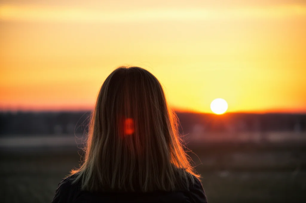 Una persona che guarda con speranza verso un orizzonte luminoso, simboleggiando il sollievo dall'emicrania cronica e dall'abuso di farmaci grazie a nuove terapie. Luce calda del tramonto, obiettivo 35mm, profondità di campo, colori caldi e rassicuranti.