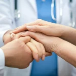 Un primo piano sulle mani di un medico che stringono delicatamente quelle di una madre in segno di conforto e supporto, in un ambiente medico ma accogliente. Obiettivo prime, 50mm, profondità di campo accentuata per mettere a fuoco le mani, illuminazione calda e soffusa, viraggio seppia e blu duotono per un effetto emotivo.