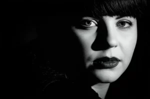 Ritratto fotografico in stile film noir di una persona il cui volto è parzialmente in ombra, simboleggiando lo stigma e le complessità psicologiche legate al sex work, obiettivo 35mm, profondità di campo.