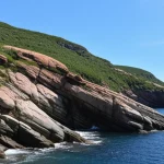 Veduta aerea di una sezione geologica degli Appalachi di Terranova, che mostra diverse formazioni di rocce ignee con colori e texture variabili. Obiettivo grandangolare, focale 18mm, luce naturale del tardo pomeriggio per esaltare i rilievi, alta definizione, focus nitido su tutta l'inquadratura.