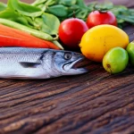 Fotografia stile still life di cibi sani e nutrienti, incluse verdure fresche colorate, frutta esotica e pezzi di pesce alla griglia che rappresentano cibi tradizionali indigeni, disposti artisticamente su un tavolo di legno rustico in una luminosa ambientazione esterna di una comunità remota australiana. Obiettivo macro 60mm, illuminazione naturale controllata per esaltare i colori, alta definizione dei dettagli del cibo.