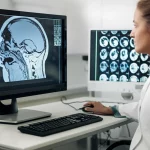 A radiologist examining MRI scans on a monitor, focusing on neck anatomy. Use case: People (portraits), Lens type: Zoom, Focal lengths: 35mm, Additional details: Precise focusing, controlled lighting, subtle depth of field.