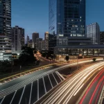 Visione aerea futuristica di una smart city al crepuscolo, con percorsi luminosi che indicano le rotte ottimizzate dei camion della spazzatura 'intelligenti' tra grattacieli illuminati e infrastrutture moderne, fotografia grandangolare 14mm, esposizione lunga per scie luminose, focus nitido sull'intera scena.