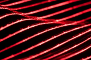 Close-up estremo, lente macro 100mm, di un tessuto flessibile con un display OLED rosso acceso integrato che mostra un motivo luminoso. Il tessuto è leggermente piegato per evidenziare la flessibilità. Illuminazione drammatica e controllata per far risaltare la luce dell'OLED e la texture del tessuto. Alta definizione, messa a fuoco precisa sull'interfaccia tra OLED e tessuto.