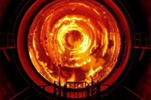 Vista interna di una caldaia industriale a combustione tangenziale durante la co-combustione di carbone e ammoniaca, fiamme intense e colorate che formano un vortice, obiettivo grandangolare 15mm per catturare l'ampiezza della fornace, lunga esposizione per accentuare il movimento delle fiamme e la luminosità, messa a fuoco nitida sulle pareti della caldaia e sulle fiamme.