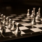 Un primo piano di una scacchiera con pezzi dorati che rappresentano gli hedge fund che muovono strategicamente contro pezzi d'argento che simboleggiano le aziende target. Profondità di campo, obiettivo prime 35mm, illuminazione drammatica con toni seppia e neri per un effetto film noir, mettendo in risalto la tensione strategica.