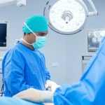 Un chirurgo pediatrico e un anestesista monitorano attentamente i parametri vitali di un piccolo paziente durante un intervento complesso di nefrectomia per tumore di Wilms, con il dispositivo SL One® visibile in background. Sala operatoria high-tech, luce focalizzata sul team e sul paziente, obiettivo prime 50mm, profondità di campo.