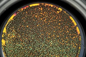 Primo piano di un film sottile di biossido di titanio modificato con nanoparticelle di palladio, depositato su vetro, che mostra un effetto iridescente sotto una luce focalizzata, suggerendo proprietà fotocatalitiche avanzate. Obiettivo macro 90mm, alta definizione, illuminazione controllata.