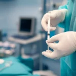 Primo piano di un anestesista che prepara con cura una siringa per l'analgesia epidurale in una sala parto moderna e luminosa, obiettivo da 35mm, profondità di campo per mettere a fuoco la siringa e le mani, sfondo leggermente sfocato con attrezzature mediche.