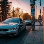 Una moderna auto elettrica in ricarica presso una colonnina in un contesto urbano rumeno al tramonto. Obiettivo prime 35mm, profondità di campo, tonalità calde e fredde (arancione e blu duotones) per un effetto suggestivo e fotorealistico.