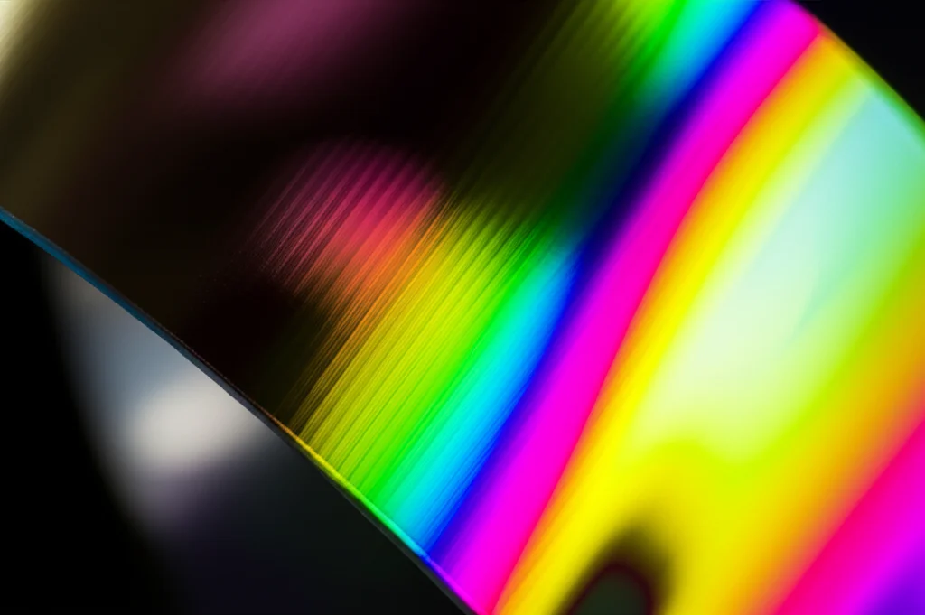 Close-up, macro photograph (60mm lens) of a thin, flexible superconducting film being gently bent. The film shows subtle rainbow interference patterns due to the strain. High detail, precise focusing, and controlled, soft studio lighting to emphasize the delicate nature of the material and the concept of bending-strain.