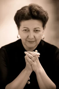 Immagine simbolica di una donna che riflette sulla sua salute, con un focus sulle mani che potrebbero essere affette da neuropatia. Fotografia ritratto, obiettivo da 35mm, bianco e nero con un tocco di colore seppia per un effetto film noir, profondità di campo per evidenziare l'espressione pensierosa.