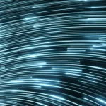 Visualizzazione artistica di un flusso di dati digitali astratti, con colori freddi come blu e argento, che si trasformano dinamicamente in una rappresentazione tridimensionale stilizzata della superficie di Fermi di un superconduttore. Particelle luminose, simboleggianti gli elettroni, si muovono senza resistenza apparente lungo questa superficie. L'immagine è catturata con un obiettivo grandangolare da 18mm, utilizzando una lunga esposizione per creare scie luminose eteree e un senso di movimento fluido, evocando la natura quantistica e l'efficienza della superconduttività.