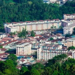 Veduta aerea di un quartiere di case popolari a Kuching, Sarawak, Malesia, con edifici densamente costruiti circondati da vegetazione tropicale lussureggiante. Wide-angle, 10-24mm, luce diurna, alta definizione, per mostrare il contesto urbano e naturale.