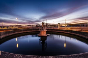 Impianto di trattamento acque reflue con focus sui serbatoi di aerazione circolari, simboleggiante lo studio sulle emissioni di N2O. Fotografia grandangolare, 10mm, lunga esposizione per acqua liscia nei serbatoi, dettagli nitidi dell'infrastruttura, cielo al crepuscolo per un effetto drammatico ma realistico, evidenziando l'importanza del controllo ambientale.