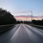 Lente grandangolare, 18 mm, un angolo leggermente basso di una moderna auto autonoma che guida su una strada asfaltata bagnata durante il giorno, una forte attenzione alla consistenza stradale e all'auto, nuvole lisce nel cielo, a lungo effetto di esposizione sulle linee stradali per suggerire il movimento.
