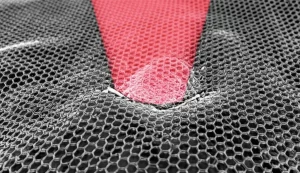 Immagine fotorealistica, stile microscopia elettronica a scansione ad alta risoluzione, che mostra nanoparticelle di ossido di grafene PEGylate (strutture lamellari sottili, leggermente rugose, di dimensioni nanometriche) adese alla superficie frastagliata di una cellula di carcinoma epatocellulare (HepG2). Un fascio di luce laser nel vicino infrarosso (NIR, 808nm), rappresentato come un cono di luce rossastra focalizzato, colpisce selettivamente le nanoparticelle, suggerendo l'attivazione per la terapia fototermica. Dettaglio elevato delle interazioni cellula-nanoparticella, illuminazione drammatica controllata per enfatizzare l'effetto del laser.