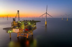 Piattaforma di produzione di idrogeno offshore illuminata al tramonto nel Mare del Nord, con turbine eoliche sullo sfondo. Grandangolo 20mm, lunga esposizione per enfatizzare le luci e l'acqua calma, focus nitido sull'impianto, cielo con colori caldi.