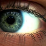 Primo piano di un occhio umano durante un esame oftalmologico, con luce focalizzata sulla pupilla e dettagli della retina visibili sullo sfondo. Obiettivo prime 35mm, profondità di campo per isolare l'occhio, illuminazione clinica.