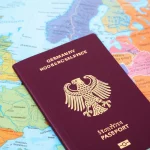 Una composizione simbolica che rappresenta la Germania moderna e multiculturale: un passaporto tedesco aperto su una mappa stilizzata dell'Europa, circondato da volti sorridenti di persone di diversa provenienza. Fotografia da ritratto, obiettivo da 35mm, luce naturale diffusa, effetto profondità di campo per mettere a fuoco il passaporto.
