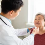Primo piano di un operatore sanitario asiatico che assiste con cura un'anziana signora cinese nel suo ambiente domestico. L'operatore sorride gentilmente mentre controlla la pressione dell'anziana, che appare serena. La luce naturale illumina la scena, creando un'atmosfera calda e rassicurante. Obiettivo da 35mm, profondità di campo per sfocare leggermente lo sfondo e mantenere il focus sui soggetti, colori naturali e vividi.