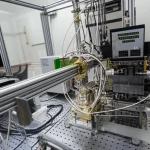 Wide-angle, 20mm, long exposure, sharp focus, un laboratorio di ottica laser avanzato con un setup di oscillatore laser a fibra monolitico in primo piano, che emette un fascio potente, stabile e di alta qualità, a simboleggiare la svolta nella mitigazione della TMI e nell'aumento di potenza.