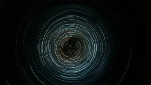 Concettualizzazione astratta delle oscillazioni chirali di una particella di Dirac, con scie luminose che rappresentano il cambiamento di chiralità nel tempo. Wide-angle, 10mm, long exposure, smooth light trails, sharp focus on a central particle representation, con un orologio stilizzato sullo sfondo a indicare il tempo finito.