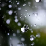 Immagine fotorealistica di gocce di pioggia che cadono su una superficie riflettente, catturate con un obiettivo macro da 100mm, alta definizione, illuminazione controllata per evidenziare la trasparenza e la forma delle gocce, con uno sfondo sfocato che suggerisce un ambiente urbano post-pioggia. L'immagine evoca precisione e dettaglio, temi centrali dell'articolo.
