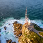 Immagine aerea mozzafiato dell'Alderney Race, con potenti correnti di marea che creano vortici e onde bianche tra la costa francese e l'isola di Alderney, un'antenna radar HF visibile su una scogliera. Fotografia paesaggistica, obiettivo grandangolare 16mm, luce del tardo pomeriggio, alta definizione, acqua dinamica.