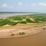 Immagine grandangolare del bacino del fiume Gange con terreni agricoli lungo le rive, evidenziando l'interfaccia tra acqua e suolo coltivato, possibile contaminazione da metalli pesanti, obiettivo grandangolare 20mm, luce naturale diffusa.