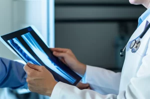 Immagine medica concettuale: un medico osserva attentamente una risonanza magnetica dell'anca di un bambino, evidenziando l'importanza della diagnostica avanzata. Luce direzionale che illumina la scansione, obiettivo prime 35mm, profondità di campo per mettere a fuoco la scansione e le mani del medico.