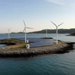 Veduta aerea di una moderna microrete su un'isola, con pannelli solari, piccole turbine eoliche, stazioni di ricarica per veicoli elettrici e un sistema di accumulo di energia visibile, il tutto integrato armoniosamente nel paesaggio. Obiettivo grandangolare 15mm, luce del tardo pomeriggio, focus nitido su tutta la scena.
