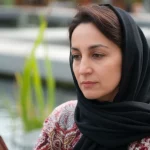 A photorealistic portrait, 35mm lens, of an Iranian woman in her late 30s, looking thoughtfully at her smartphone screen, with a subtle depth of field blur of environmental elements like water or plants in the background.
