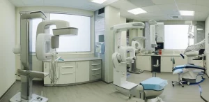 Wide-angle landscape, 20mm lens, vista panoramica all'interno di una clinica di implantologia dentale moderna e luminosa, che mostra attrezzature avanzate come scanner CBCT e setup chirurgico, messa a fuoco nitida, rappresentando l'ambiente per procedure avanzate di rigenerazione ossea.