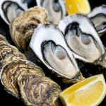 Un vassoio di ostriche freschissime aperte, pronte per essere gustate, presentate con spicchi di limone. Macro lens, 85mm, high detail, precise focusing, controlled lighting, con una leggera condensa sulle conchiglie che ne indica la freschezza.