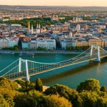 Veduta aerea di Budapest con evidenziati in verde brillante parchi urbani, tetti verdi e corridoi ecologici lungo il Danubio, integrati armoniosamente nel tessuto cittadino. Obiettivo grandangolare 24mm, luce dorata del tardo pomeriggio, alta definizione per mostrare i dettagli delle soluzioni basate sulla natura e l'interazione tra ambiente costruito e naturale.