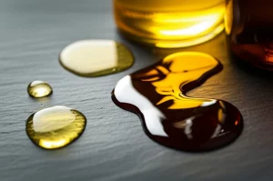 Fotografia macro ad alta definizione di gocce di oli essenziali diversi (rosmarino color ambra chiaro, origano dorato, chiodi di garofano marrone scuro) che si mescolano delicatamente su una superficie di ardesia scura, obiettivo macro 105mm, illuminazione controllata da studio che esalta i colori caldi, la viscosità e la texture oleosa, simboleggiando la sinergia e la potenza naturale.