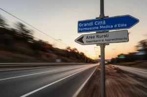 Un bivio stradale con un cartello che indica 'Grandi Città - Formazione Medica d'Elite' e un altro, più piccolo e meno curato, 'Aree Rurali - Opportunità di Apprendimento'. Telephoto zoom, 100mm, fast shutter speed per catturare un momento di scelta, luce del tardo pomeriggio che crea lunghe ombre e un'atmosfera di dilemma.