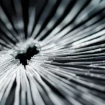 Immagine fotorealistica, macro lens, 70mm, high detail, controlled lighting. Una crepa in un materiale trasparente simile a vetro polimerico si sta visibilmente chiudendo. Linee sottili di motion blur indicano l'effetto delle vibrazioni indotte che stanno guarendo la fessura. La messa a fuoco è nitida sull'interfaccia in via di guarigione, con il resto del materiale leggermente fuori fuoco per profondità di campo.