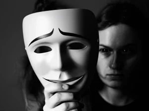 Un primo piano drammatico di una maschera sorridente tenuta davanti a un volto triste e pensieroso, simboleggiando la depressione nascosta. Illuminazione da film noir, bianco e nero con un accenno di blu duotone, obiettivo da 35mm, profondità di campo per mettere a fuoco la maschera e sfocare leggermente il volto reale.