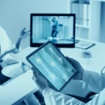 Fotografia realistica di un medico reumatologo che esamina i referti di un paziente con artrite reumatoide su un tablet, mentre sullo sfondo si vede una paziente che interagisce con lui tramite uno schermo per una visita virtuale. L'ambiente è uno studio medico moderno. Obiettivo prime 35mm, profondità di campo, illuminazione controllata, duotone blu e argento per un look tecnologico ma umano.