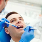 Un dentista, indossando guanti e mascherina, applica con precisione una formulazione viscosa di blu di metilene di un intenso colore blu su un dente di un paziente sdraiato sulla poltrona dentistica. L'ambiente è uno studio dentistico moderno, ben illuminato, con attrezzature specialistiche visibili sullo sfondo. Fotografia di ritratto, obiettivo prime 35mm, profondità di campo che mette a fuoco l'applicazione del gel sul dente, lasciando lo sfondo leggermente sfocato.