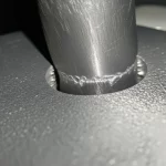 Close-up, macro lens, 100mm, di un componente in lega di alluminio AA5083-Sc prodotto con manifattura additiva mentre subisce un processo di ossidazione anodica in una soluzione di nitrato di cerio, con elettrodi visibili e leggero sviluppo di bollicine, alta definizione, messa a fuoco precisa, illuminazione controllata da laboratorio.