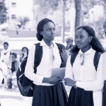 Fotografia di un gruppo di giovani studentesse universitarie etiopi, diverse tra loro, in un campus all'aperto. Alcune conversano, altre appaiono riflessive. Obiettivo da ritratto 35mm, luce naturale, profondità di campo, per trasmettere un senso di comunità e le preoccupazioni individuali sottostanti. Viraggio blu e grigio.