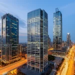 Fotografia grandangolare di uno skyline urbano al crepuscolo, con grattacieli dalle architetture complesse e multiscala in primo piano che riflettono le luci della città, obiettivo grandangolare 14mm, lunga esposizione per scie luminose del traffico e nuvole mosse, messa a fuoco nitida sugli edifici, atmosfera vibrante e moderna.