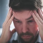 A person, mid-migraine attack, holding their head, 35mm portrait, depth of field, showing the physical and emotional toll.
